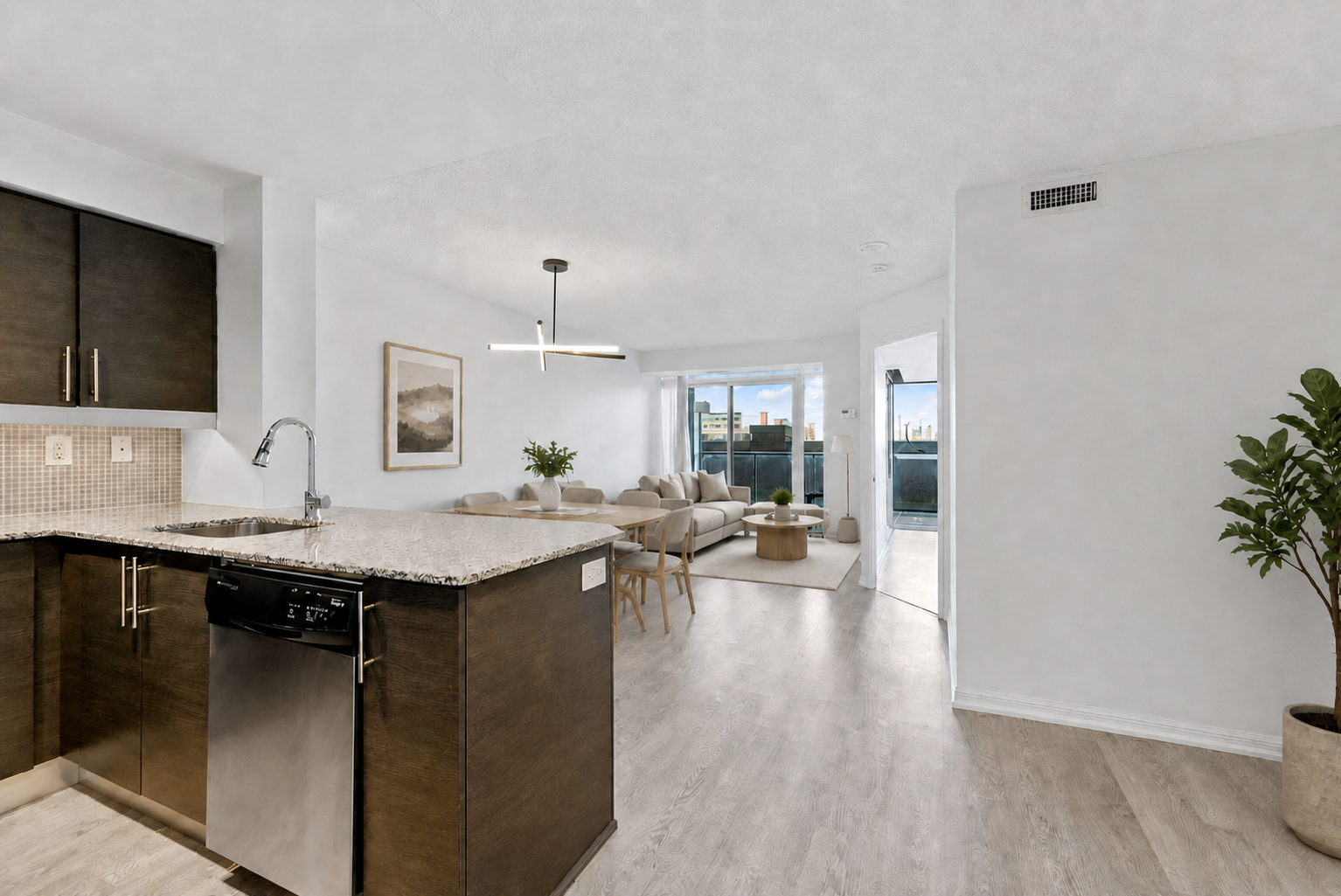 Open-concept kitchen and living area: dark wood cabinets, granite island with sink and dishwasher, leading to a light living room with a beige sofa and large windows.