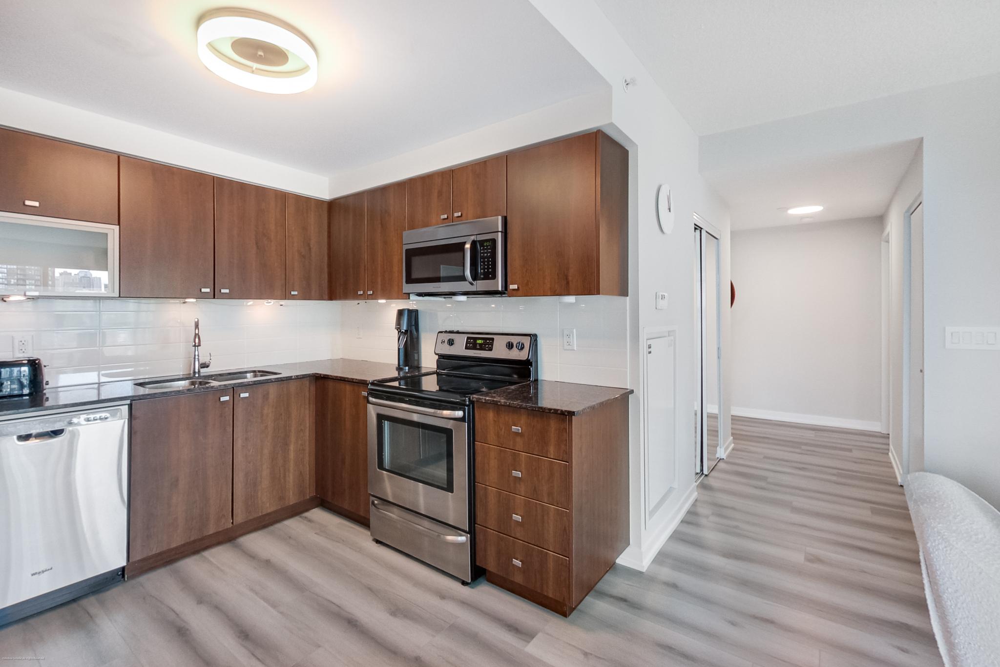 3 | Liberty Village Toronto | Your Online Neighbourhood Guide Modern kitchen with dark wood cabinets, stainless steel stove and microwave, gray countertops, and light wood flooring.