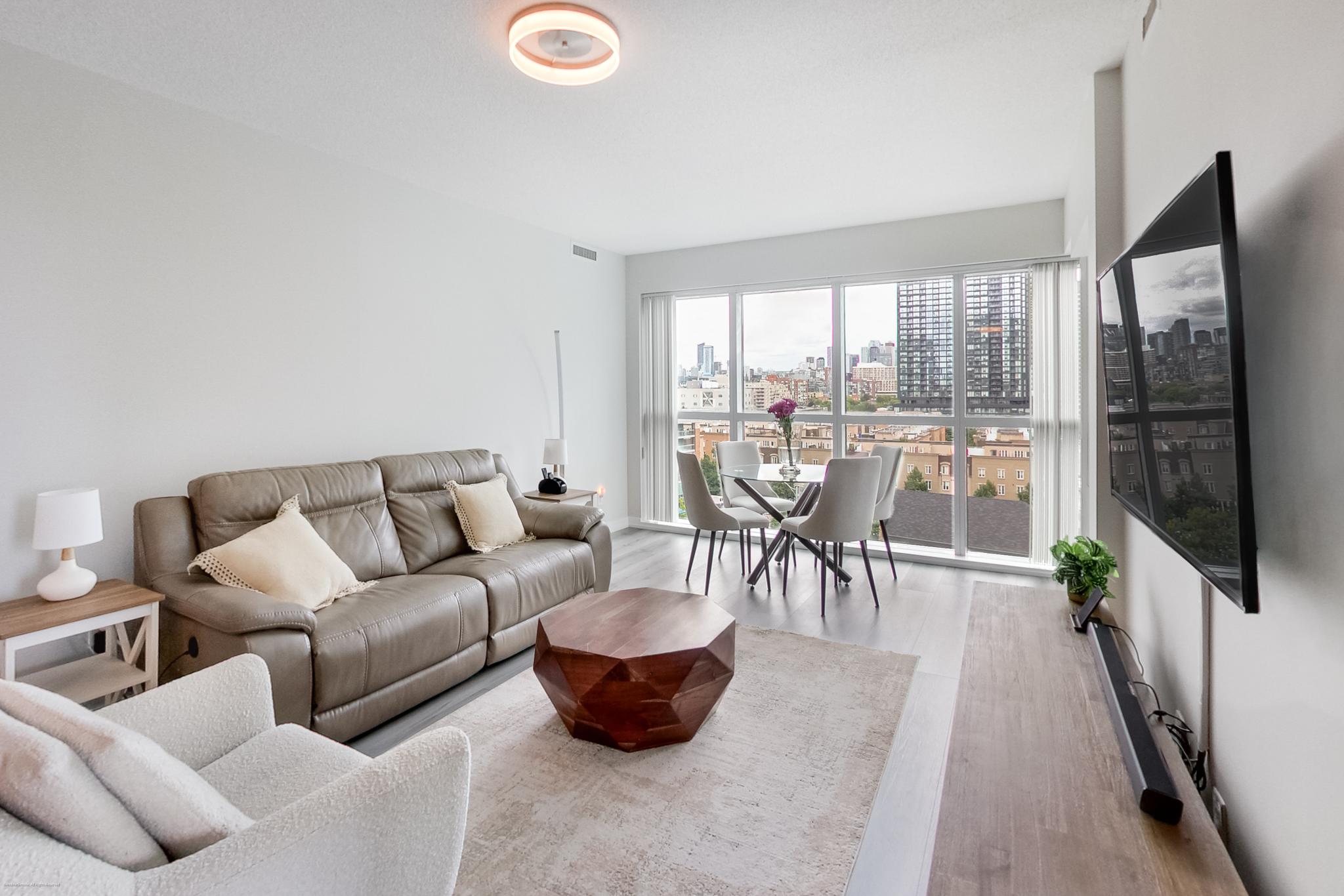 8 | Liberty Village Toronto | Your Online Neighbourhood Guide Bright modern living room with beige leather sofa, white chairs, and a glass dining table by large windows overlooking the city skyline.