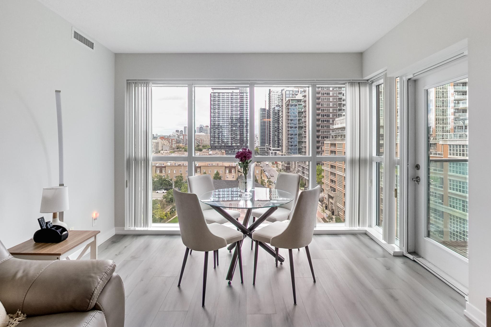904-69 Lynn Williams | Liberty Village Toronto | Your Online Neighbourhood Guide Dining area with glass round table and beige chairs, by floor-to-ceiling windows overlooking a city skyline.
