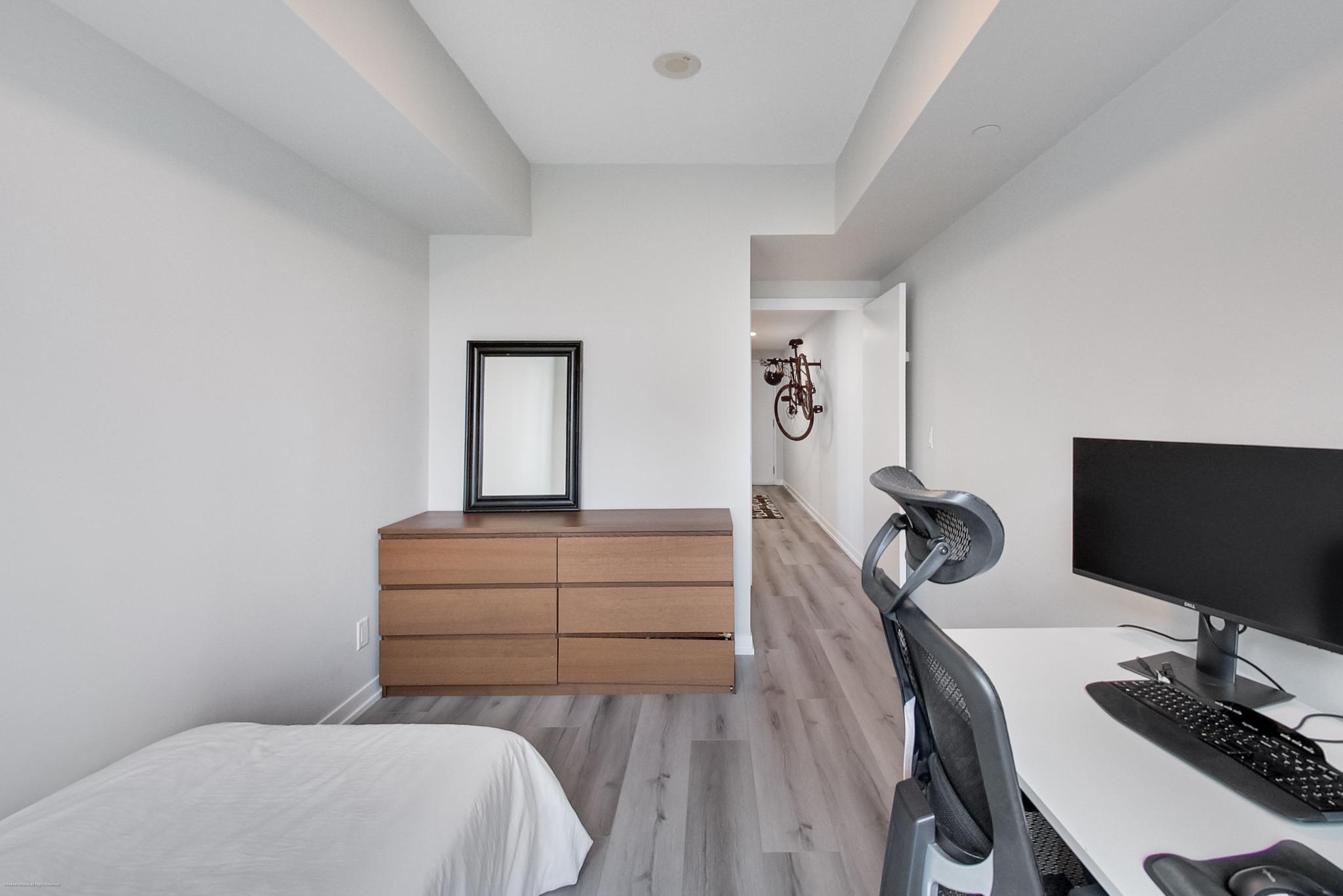19 | Liberty Village Toronto | Your Online Neighbourhood Guide Modern bedroom with a white desk and computer setup; hallway at back shows a bicycle mounted on the wall.