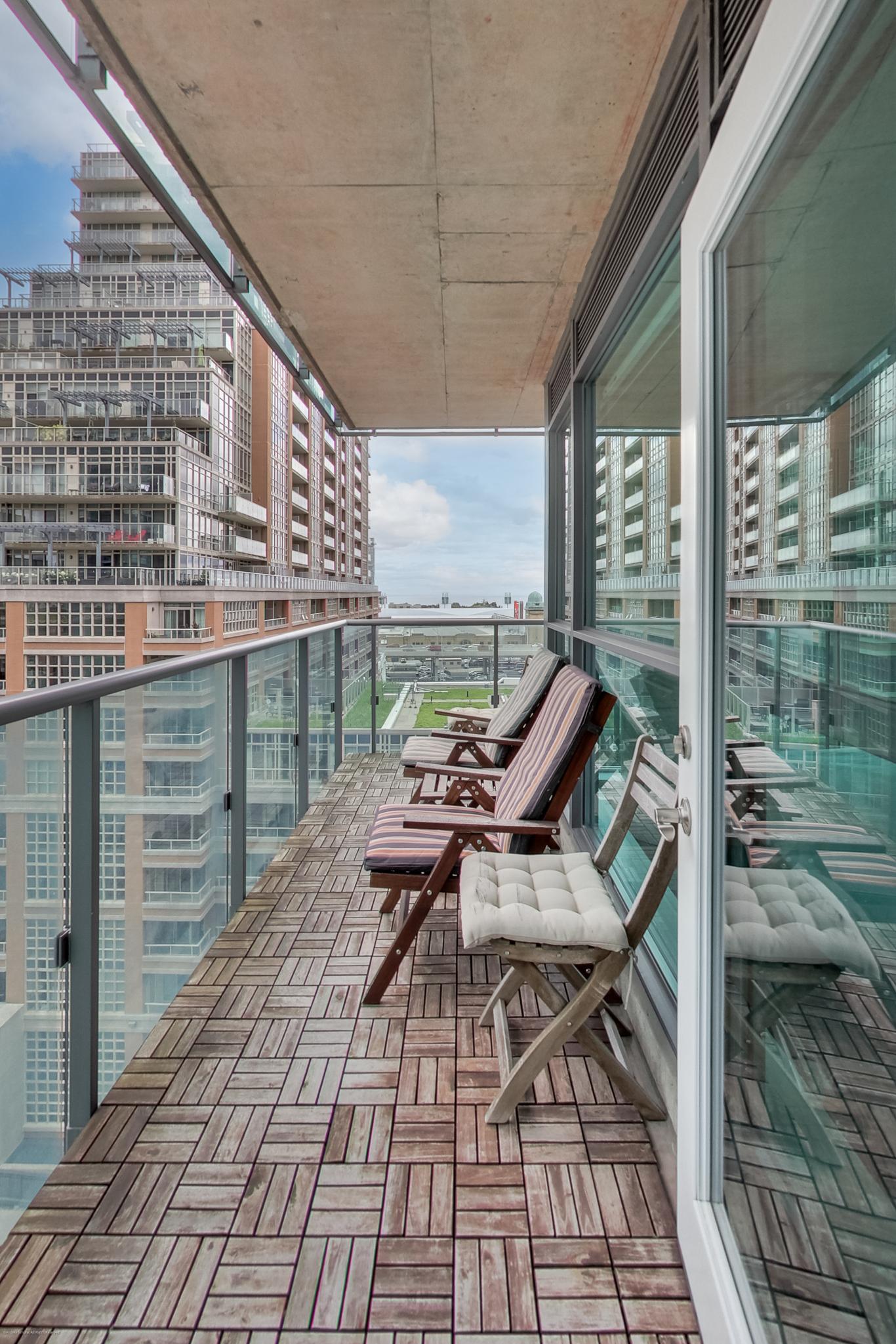 20 | Liberty Village Toronto | Your Online Neighbourhood Guide Balcony with wooden tile floor and glass railing, facing modern apartment buildings and a street below.