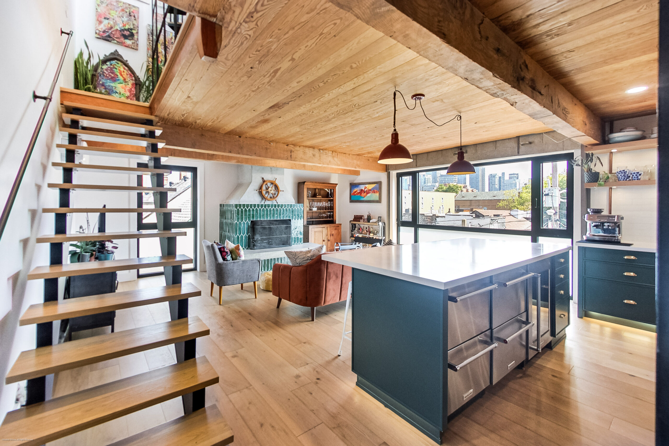 6 Littlehayes | Liberty Village Toronto | Your Online Neighbourhood Guide Open-concept living space with a blue kitchen island, wooden staircase, and large windows showing the city skyline.