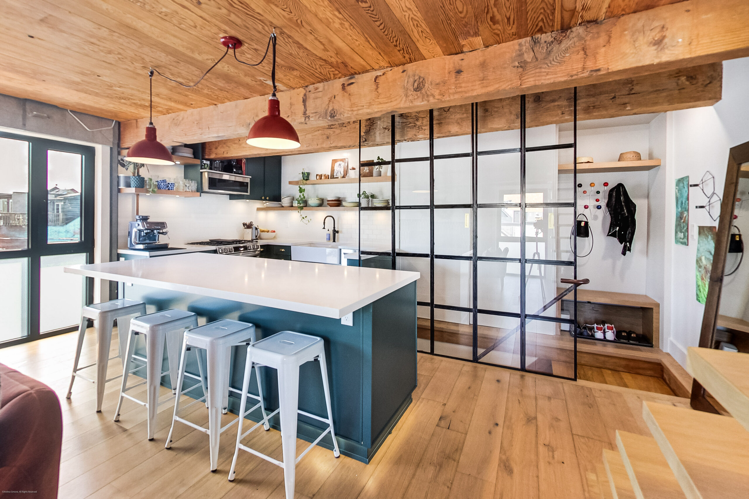 andreasimonecom | Liberty Village Toronto | Your Online Neighbourhood Guide Open-concept kitchen with teal island, white countertops, and a black metal-framed glass divider under a wooden beam ceiling with red pendant lights.