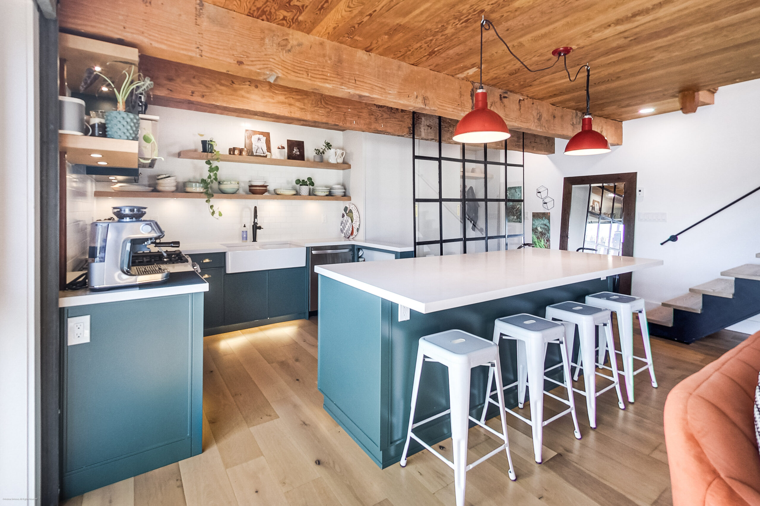 andreasimonecom | Liberty Village Toronto | Your Online Neighbourhood Guide Open-concept kitchen with teal cabinets, white countertops, a long island, and white bar stools under exposed wooden beams and red pendant lights.