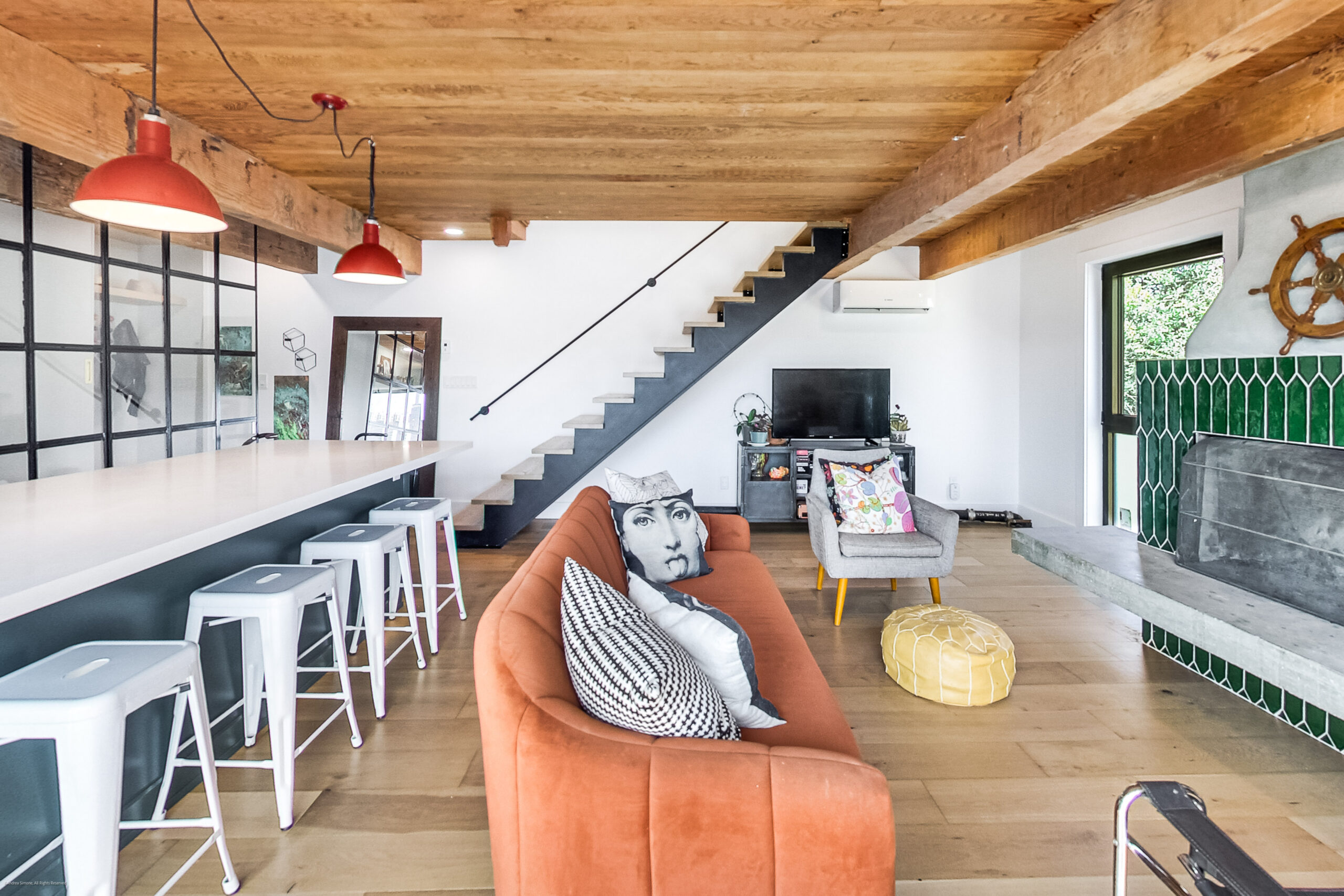 andreasimonecom | Liberty Village Toronto | Your Online Neighbourhood Guide Loft-style living room with orange sofa, colorful cushions, and a staircase along a white wall under exposed wooden beams.