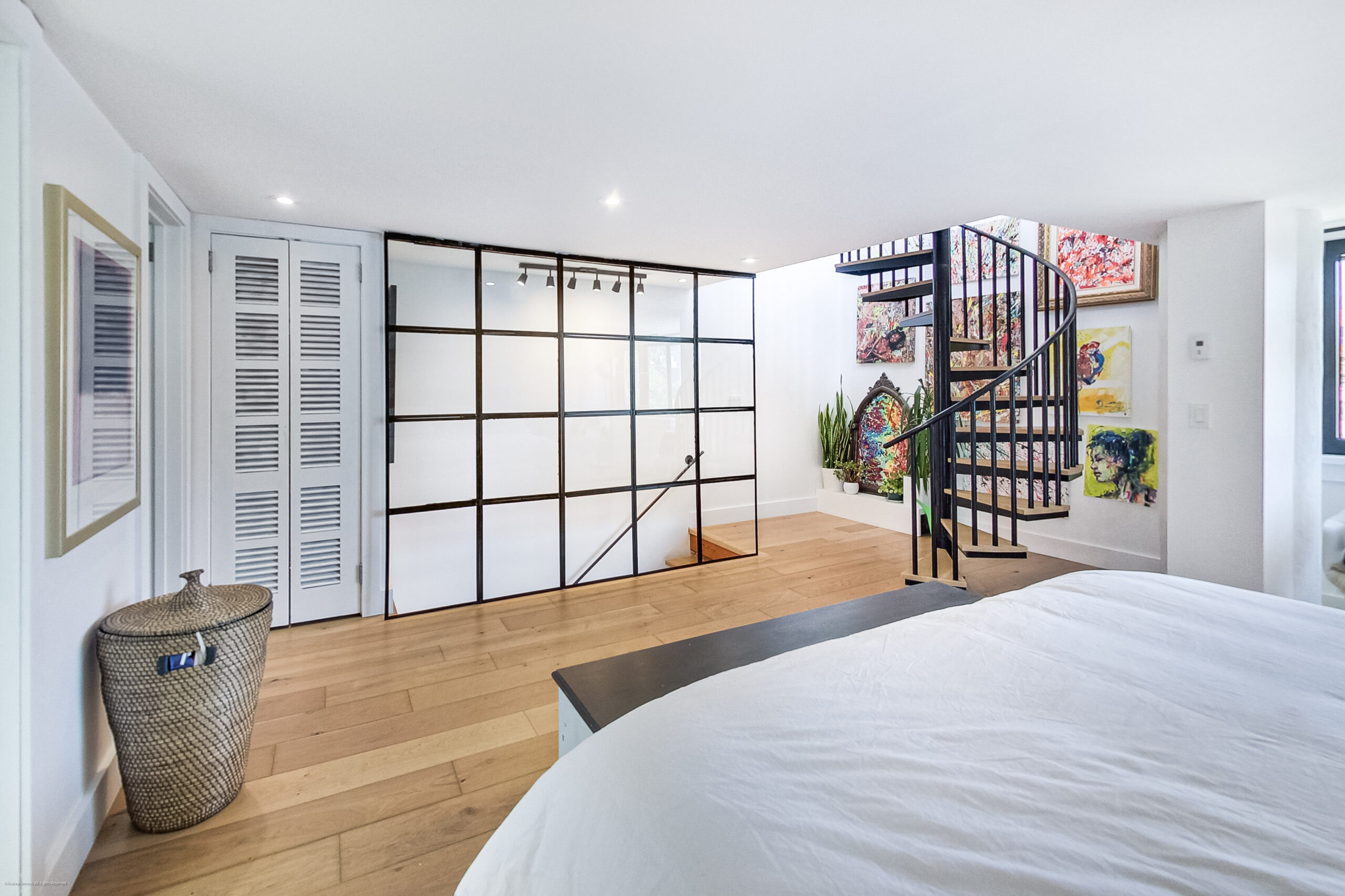 andreasimonecom | Liberty Village Toronto | Your Online Neighbourhood Guide Bright modern bedroom featuring a glass-paneled divider, a black spiral staircase, and vibrant wall art beside a white bed and wooden floor.