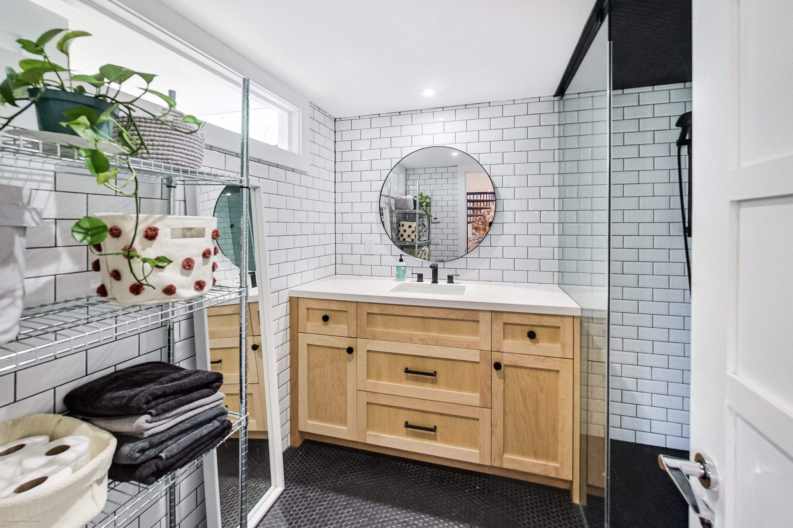 andreasimonecom | Liberty Village Toronto | Your Online Neighbourhood Guide Modern bathroom with a light wood vanity, round mirror, white subway tile walls, and a potted plant on a metal shelf.