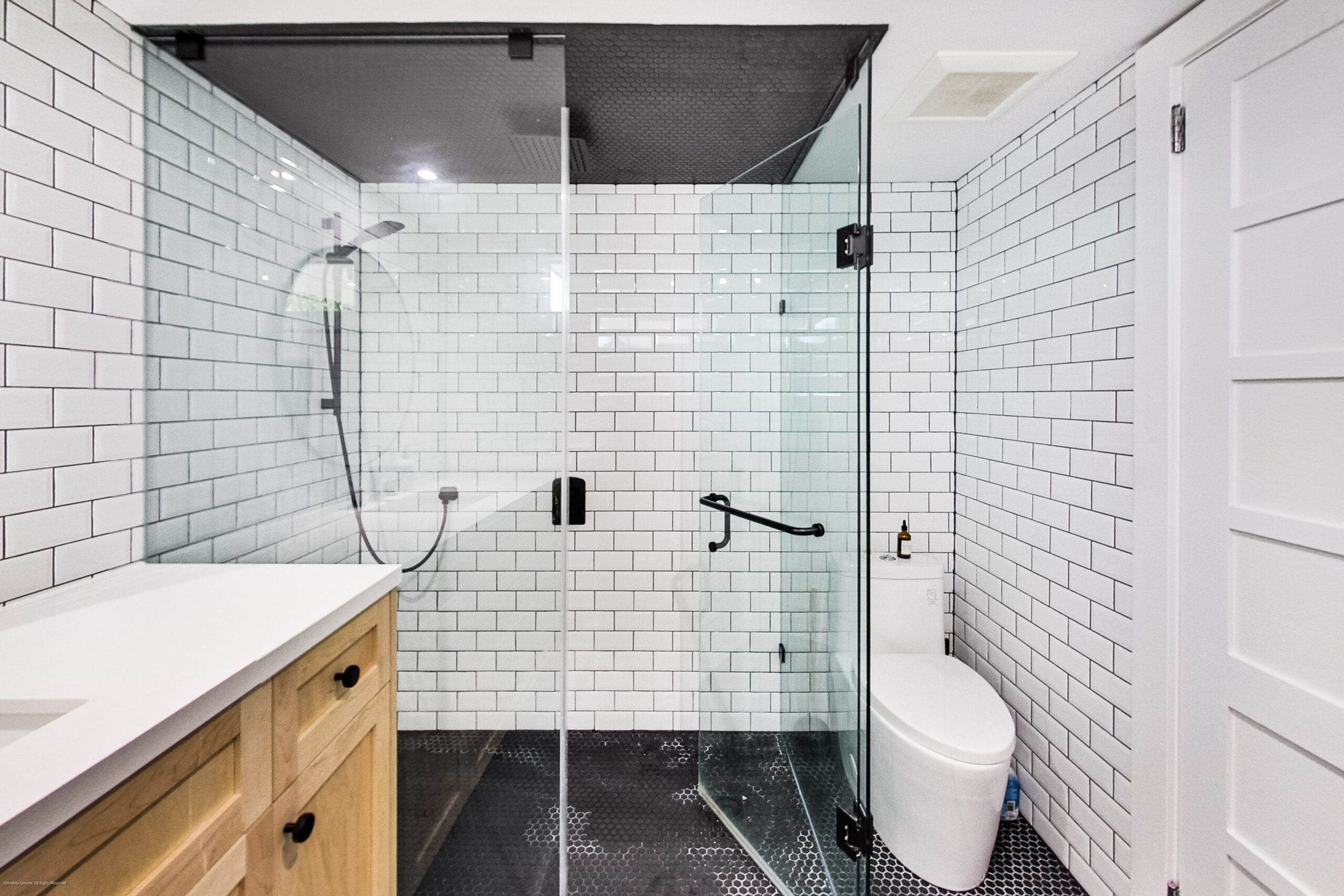 andreasimonecom | Liberty Village Toronto | Your Online Neighbourhood Guide Modern bathroom with a glass shower enclosure, white subway tiles, and a wooden vanity on the left.